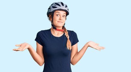 Beautiful caucasian woman wearing bike helmet clueless and confused expression with arms and hands...