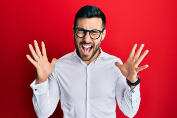 Naklejka premium Young hispanic businessman wearing shirt and glasses celebrating mad and crazy for success with arms raised and closed eyes screaming excited. winner concept