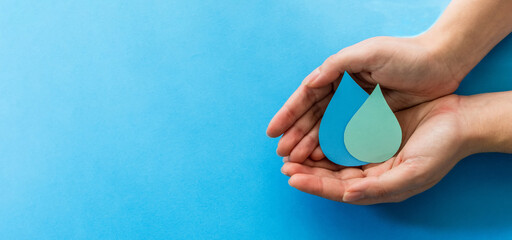 Woman hands holding paper cut water drop on blue background. Clean water and sanitation, saving...