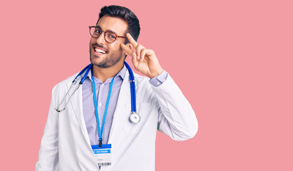 Young hispanic man wearing doctor uniform and stethoscope doing peace symbol with fingers over...