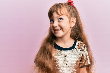 Little caucasian girl kid wearing festive sequins dress looking away to side with smile on face, natural expression. laughing confident.