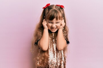 Little caucasian girl kid wearing festive sequins dress covering ears with fingers with annoyed expression for the noise of loud music. deaf concept.