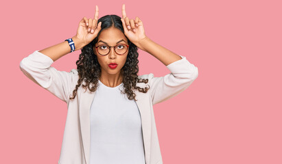 Fototapeta premium Young african american girl wearing business clothes doing funny gesture with finger over head as bull horns