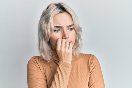 Young blonde girl wearing casual clothes looking stressed and nervous with hands on mouth biting nails. anxiety problem.