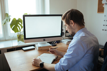 Man working from a home office. Computer with blank empty screen for copy space and information. A...