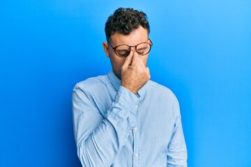Fototapeta premium Young hispanic man wearing casual clothes and glasses tired rubbing nose and eyes feeling fatigue and headache. stress and frustration concept.