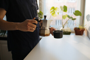 Man making morning coffee in moka espresso pot. Flavorful coffee at home kitchen. Male pouring coffee in a cup. Guy morning cozy ritual. Breakfast lighter roast blend. Home leisure fika at holidays