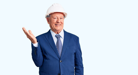 Senior handsome grey-haired man wearing suit and architect hardhat smiling cheerful presenting and pointing with palm of hand looking at the camera.