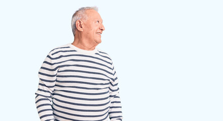 Obraz premium Senior handsome grey-haired man wearing casual striped sweater looking away to side with smile on face, natural expression. laughing confident.