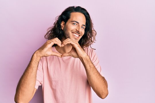 Young handsome man with long hair wearing casual clothes smiling in love doing heart symbol shape with hands. romantic concept.