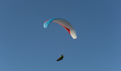 A beautiful view of a paraglide flying gliding on a clear blue sky at the golden hour with a nice wind windy breeze on a sunny day 