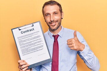 Young handsome man holding clipboard with contract document smiling happy and positive, thumb up doing excellent and approval sign
