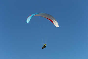 A beautiful view of a paraglide flying gliding on a clear blue sky at the golden hour with a nice wind windy breeze on a sunny day 