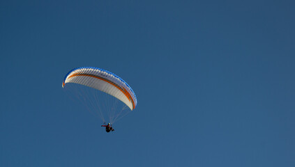 A beautiful view of a paraglide flying gliding on a clear blue sky at the golden hour with a nice wind windy breeze on a sunny day 
