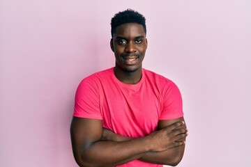 Handsome black man wearing casual pink t shirt happy face smiling with crossed arms looking at the camera. positive person.