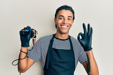 Young handsome african american man tattoo artist wearing professional uniform and gloves holding...