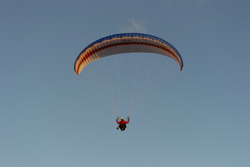 A beautiful view of a paraglide flying gliding on a clear blue sky at the golden hour with a nice wind windy breeze on a sunny day 
