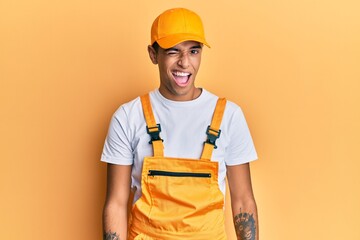 Young handsome african american man wearing handyman uniform over yellow background winking looking at the camera with sexy expression, cheerful and happy face.