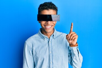Naklejka premium Young handsome african american man wearing banner glasses covering eyes surprised with an idea or question pointing finger with happy face, number one