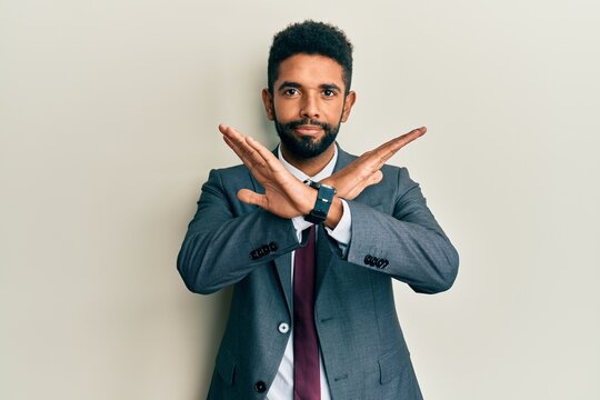 Handsome hispanic man with beard wearing business suit and tie rejection expression crossing arms doing negative sign, angry face