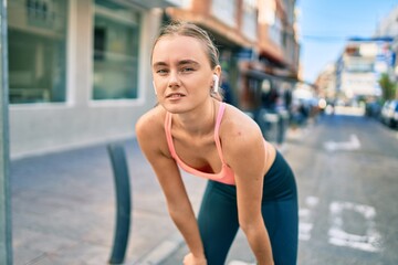 Young blonde sportswoman tired resting with hands on knees at the city.