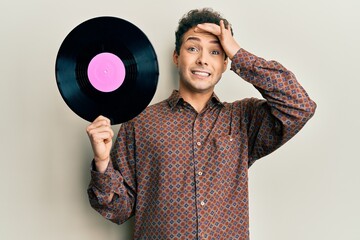 Young handsome man holding vinyl disc stressed and frustrated with hand on head, surprised and angry face