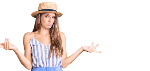 Young beautiful blonde woman wearing summer hat clueless and confused with open arms, no idea concept.