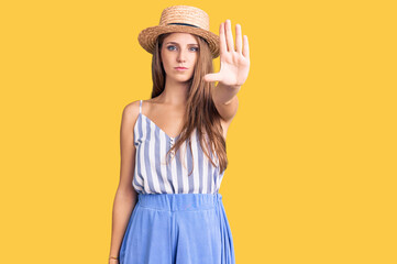 Young beautiful blonde woman wearing summer hat doing stop sing with palm of the hand. warning expression with negative and serious gesture on the face.