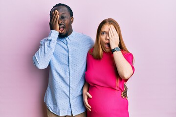 Young interracial couple expecting a baby, touching pregnant belly yawning tired covering half face, eye and mouth with hand. face hurts in pain.