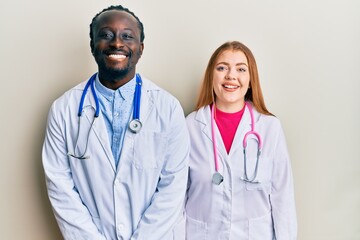 Fototapeta premium Young interracial couple wearing doctor uniform and stethoscope with a happy and cool smile on face. lucky person.