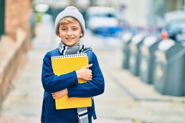 Adorable blond student kid smiling happy holding book at the school.