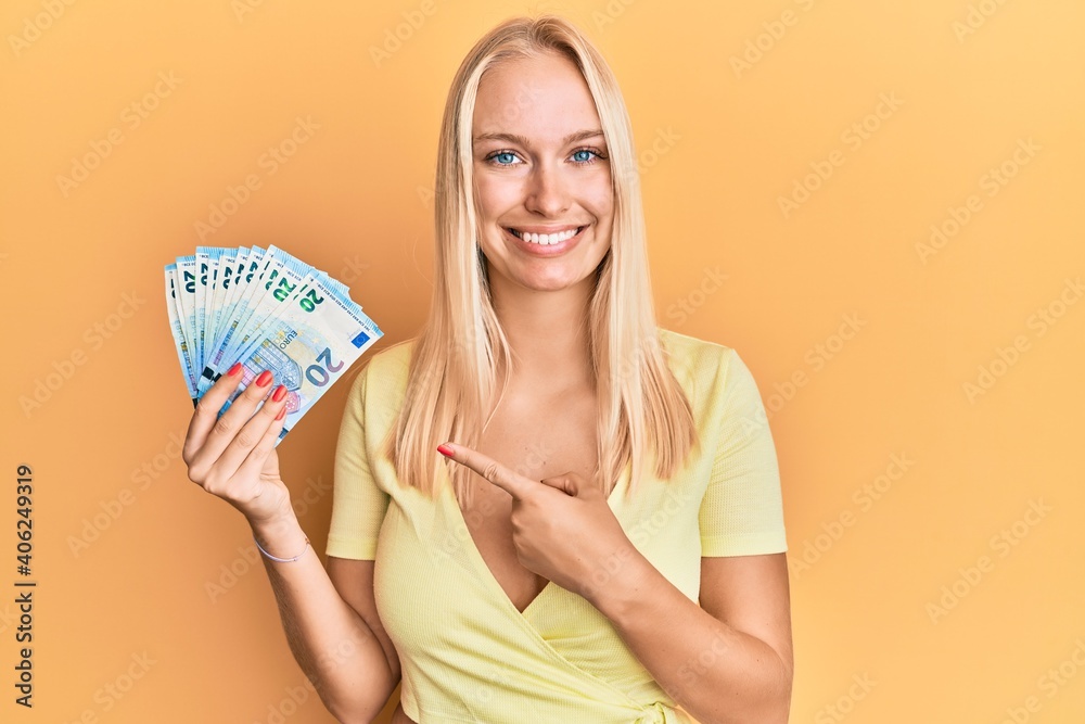 Wall mural Young blonde girl holding 20 euro banknotes smiling happy pointing with hand and finger