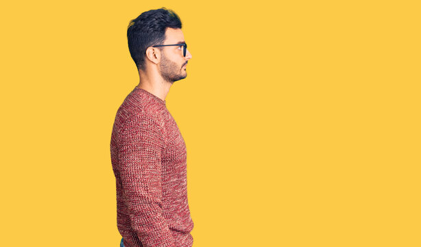 Young handsome hispanic man wearing winter sweater and glasses looking to side, relax profile pose with natural face with confident smile.
