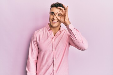 Hispanic young man wearing casual clothes doing ok gesture with hand smiling, eye looking through fingers with happy face.