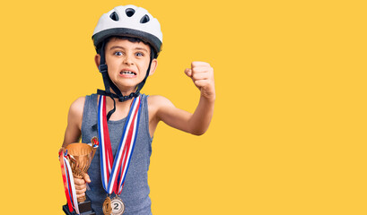 Little cute boy kid wearing bike helmet and winner medals holding winner trophy annoyed and...