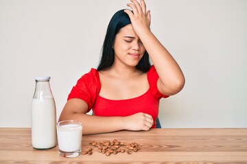 Young asian girl drinking healthy almond milk surprised with hand on head for mistake, remember error. forgot, bad memory concept.