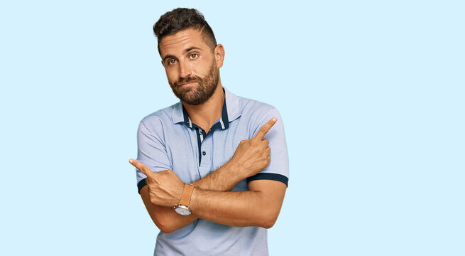 Handsome man with beard wearing casual clothes pointing to both sides with fingers, different direction disagree