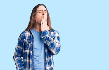 Young adult man with long hair wearing casual shirt bored yawning tired covering mouth with hand. restless and sleepiness.