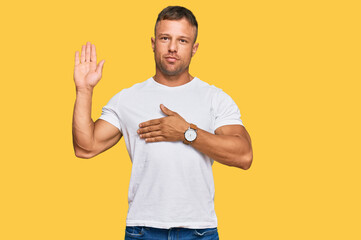 Handsome muscle man wearing casual white tshirt swearing with hand on chest and open palm, making a...