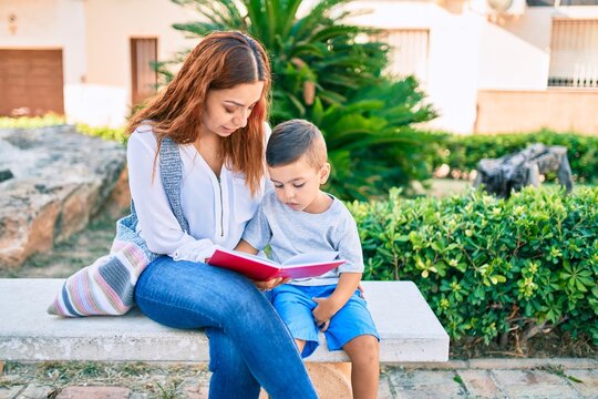 Adorable latin mother and son sitting on the bench and reading book at the park.