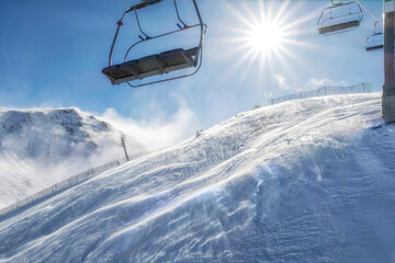 Chairlift from a ski resort on a sunny day with the sun in the background and a blizzard breeze on...