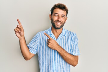 Handsome man with beard wearing casual shirt smiling and looking at the camera pointing with two hands and fingers to the side.