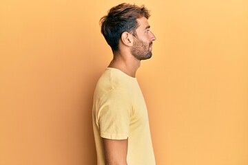Handsome man with beard wearing casual yellow tshirt over yellow background looking to side, relax profile pose with natural face with confident smile.