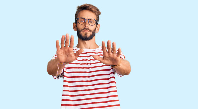 Handsome blond man with beard wearing casual clothes and glasses doing stop gesture with hands palms, angry and frustration expression