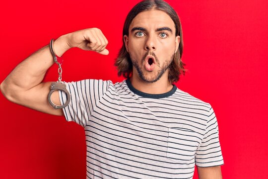 Young handsome man wearing prisoner handcuffs scared and amazed with open mouth for surprise, disbelief face