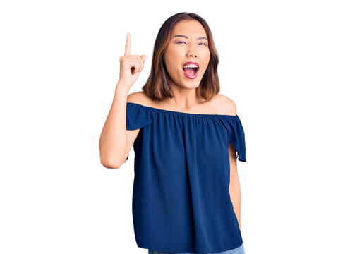 Young beautiful chinese girl wearing casual clothes pointing finger up with successful idea. exited and happy. number one.