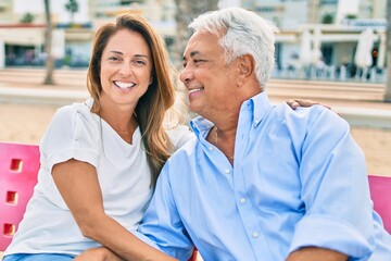 Obraz premium Middle age hispanic couple smiling happy and hugging sitting on bench at the beach.
