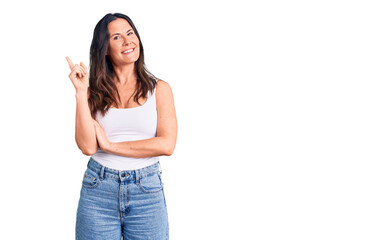 Young beautiful brunette woman wearing casual sleeveless t-shirt with a big smile on face, pointing with hand and finger to the side looking at the camera.