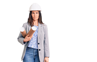 Young beautiful brunette woman wearing architect hardhat holding blueprint thinking attitude and...