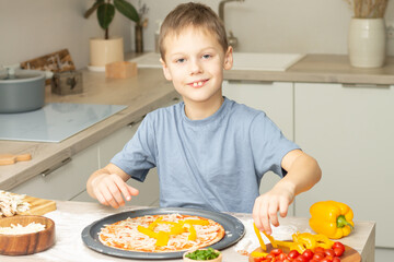 Boy 7-10 in T-shirt cooking pizza in kitchen. Kid smiles and cooks